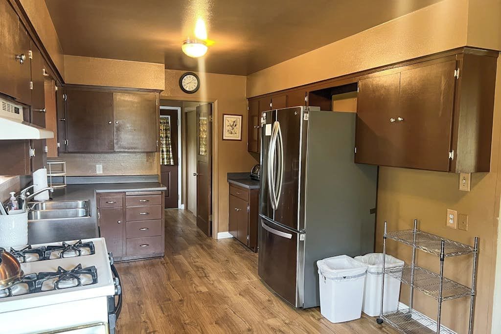 A kitchen with a stove, refrigerator, wooden cabinets, and a metal shelf.