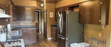 A kitchen with a stove, refrigerator, wooden cabinets, and a metal shelf.