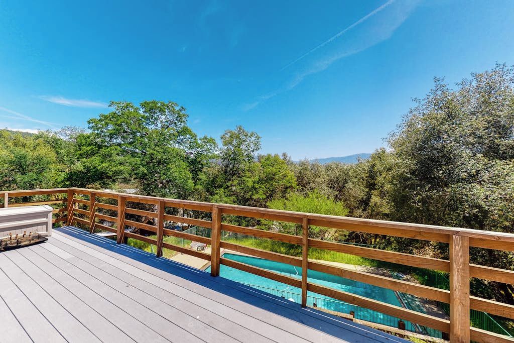 Une terrasse en bois avec une piscine, entourée de verdure et d’arbres.