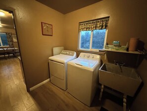 A laundry room with two washing machines, a sink, and a window with a view. - Hodges Hill Yosemite House (Oakhurst)