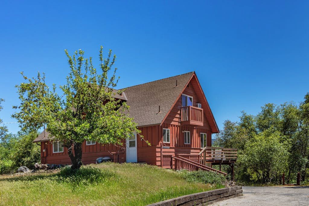 Une maison en bois rouge avec un balcon, entourée de verdure et sous un ciel dégagé.