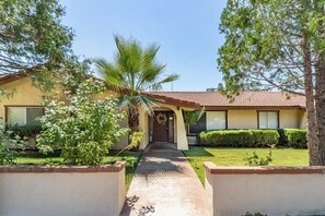 A residential property with a paved driveway leading to a front door, surrounded by greenery and a palm tree. - Putney Place - Hot Tub & Mountain Views (North Fork)