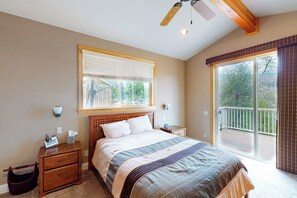Ein Schlafzimmer mit Bett, Nachttisch, Holz-Kopfteil, Fenster mit Jalousien, Deckenventilator und einer Schiebetür zu einem Balkon.