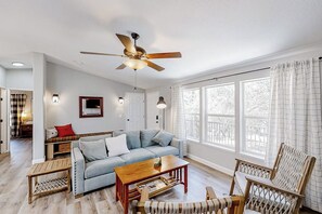 A spacious living room with a sofa, coffee table, and wicker chairs. A ceiling fan is visible, and there are windows with curtains. - Out in the Wild - Near Bass Lake & Dog-Friendly (Oakhurst)