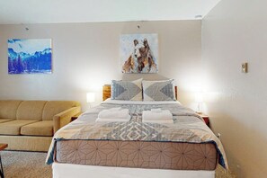 A bedroom with a bed, two paintings, a sofa, and a nightstand with a lamp.