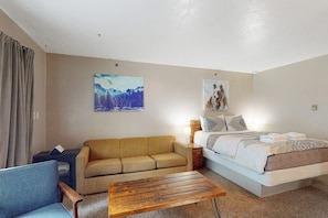 A hotel room with a bed, a sofa, a coffee table, and two paintings on the wall.