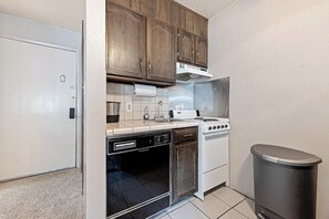 Une cuisine de taille réduite, dotée de meubles en bois, d’un lave-vaisselle, d’une cuisinière et d’une poubelle.