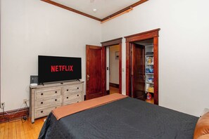 A bedroom with a bed, a dresser, a television displaying 'NETFLIX', and a closet with shelves. - 1BR I Roberts Loft #2, Walk to DT, Queen, W/D (Fargo)