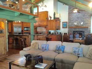 A spacious living area with a high ceiling, a fireplace, and a kitchen with wooden cabinets. - Knott Lakeview - Lake Views, Boat Slip & Dogs OK (Bass Lake)