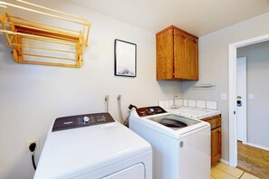 Ein Waschraum mit einer Waschmaschine und einem Trockner mit Frontlader, Holzschränken, einem Wäscheständer und einem gerahmten Bild an der Wand.