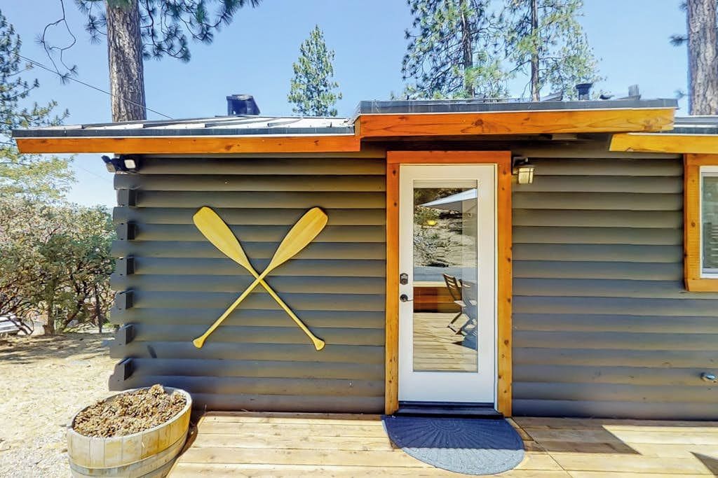 Una cabaña con puerta de madera, una terraza y una pala apoyada en la pared.