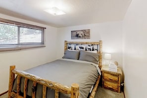 Ein Schlafzimmer mit einem hölzernen Bettgestell, einer grauen Bettdecke, einem Nachttisch mit einer Lampe und einem Bärenbild an der Wand.