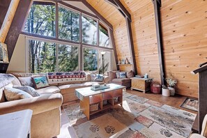 A cozy cabin interior with a large window, wooden walls, a sofa, a coffee table, and a lamp. - Chief Peak Cabin - Near Yosemite, Deck & Loft (Fish Camp)