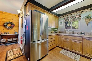 A kitchen with wooden cabinets, a stainless steel refrigerator, a sink, and a decorative wall. - Chief Peak Cabin - Near Yosemite, Deck & Loft (Fish Camp)