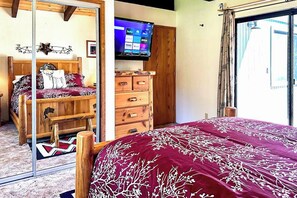 Ein Schlafzimmer mit einem Bett, einer Kommode, einem an der Wand befestigten Fernseher und einer Glastür zu einem Außenbereich.
