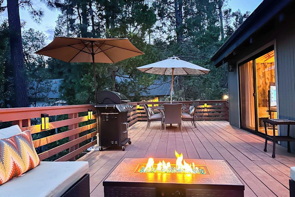 Eine Terrasse mit Feuerstelle, Gartenmöbeln und Sonnenschirmen.