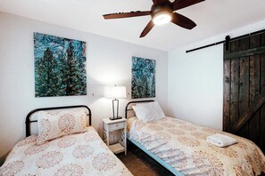 Habitació amb dos llits, un ventilador de sostre i obres d'art a les parets.