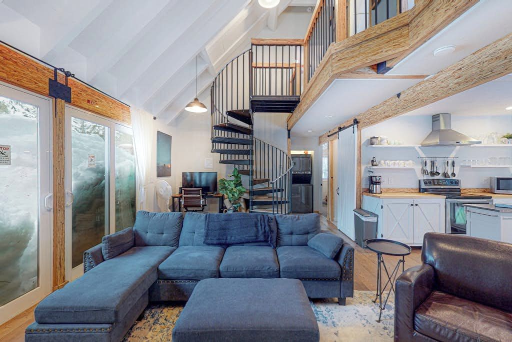 A modern interior with a large sectional sofa, a staircase, and a kitchen area.