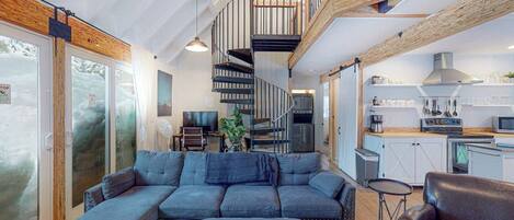 A modern interior with a large sectional sofa, a staircase, and a kitchen area.
