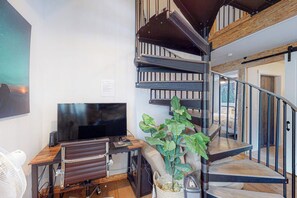 A modern living room with a flat-screen TV, a wooden coffee table, a leather sofa, a large potted plant, and a spiral staircase. - Starfall - Modern Yosemite Home, Great Deck (Yosemite West)