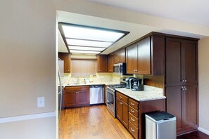 Una cocina con armarios de madera, un refrigerador de acero inoxidable, un lavavajillas y un microondas.