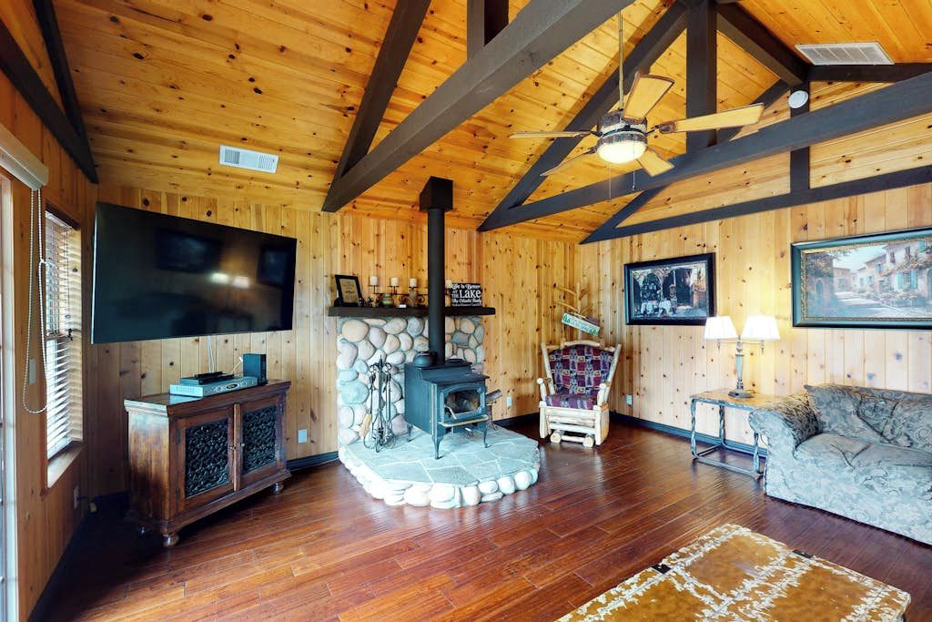 A cozy cabin interior with a stone fireplace, wooden walls, a flat-screen TV, and a comfortable seating area.