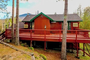 A wooden cabin with a red exterior, a covered deck, and a mountain backdrop. - Calandri Lakeview House (Bass Lake)
