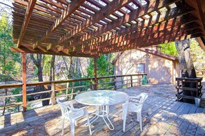 An outdoor patio with a wooden pergola, a round glass table, and white plastic chairs. - Lancaster Cabin - Bass Lake, Fireplace & Deck (Bass Lake)