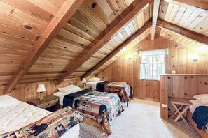 A cozy attic bedroom with wooden walls and sloped ceilings, featuring two beds with quilts and a small table. - Lancaster Cabin - Bass Lake, Fireplace & Deck (Bass Lake)