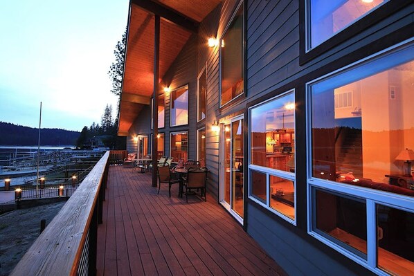 Una terraza de madera con mobiliario exterior, ventanas amplias y vista al agua.