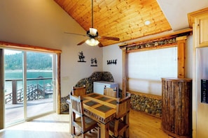 A wooden interior with a dining table, chairs, a ceiling fan, a refrigerator, and a view of a body of water through large windows. - Humphreys Lakefront - Private Dock, Sleeps 24 (Bass Lake)
