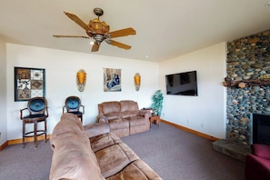 A living room with a large sectional sofa, two armchairs, a ceiling fan, a flat-screen TV, and a stone fireplace. - Humphreys Lakefront - Private Dock, Sleeps 24 (Bass Lake)