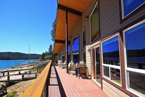 Terraza de madera con mobiliario exterior con vistas a un cuerpo de agua y colinas.