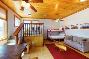 Una habitación con techo de madera, una cama litera, un sofá, una mesa de comedor y una escalera.