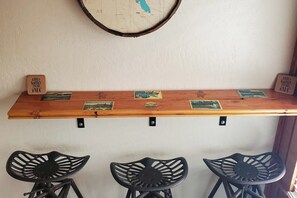 Eine Bar mit einer Holztrennwand, die verschiedene Gegenstände zeigt, und drei schwarzen Barhocker.