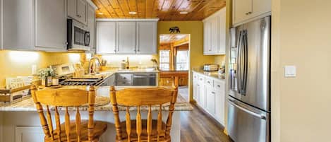 Una cocina con techo de madera, armarios blancos, electrodomésticos de acero inoxidable y dos sillas de madera.