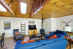 Ein gemütliches Wohnzimmer mit Holzboden, einer Couch, einem Fernseher und einem Kamin.