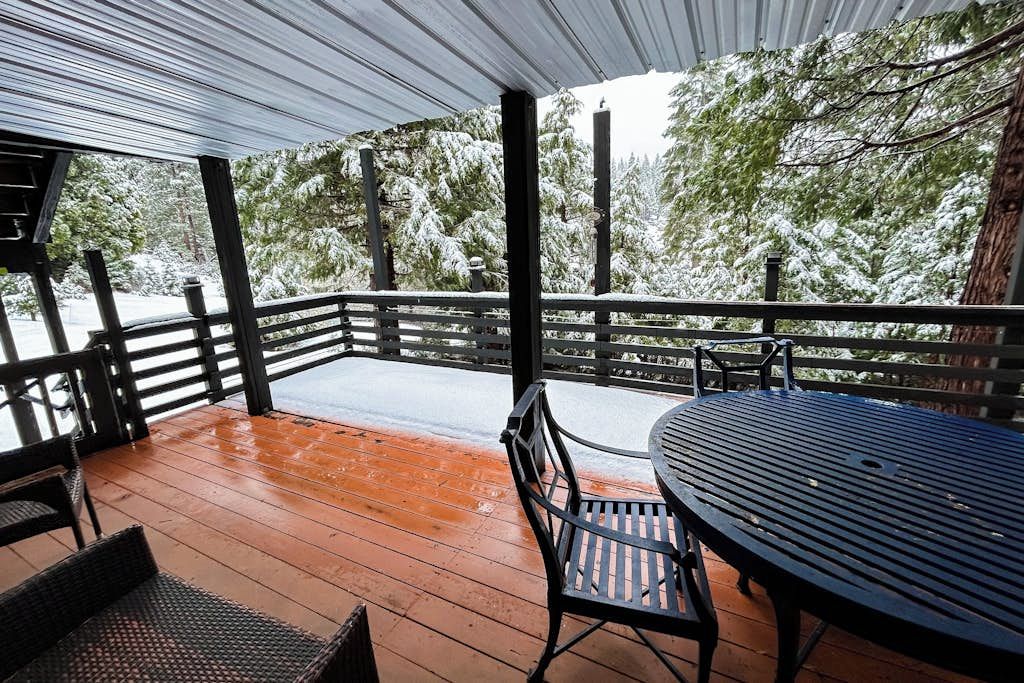 Un espace extérieur abrité, doté d’une terrasse en bois, d’une rambarde en métal et d’une table avec des chaises.