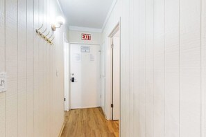 Ein Flur mit einer weißen Tür, auf der 'EXIT' steht, und einem Schild, das die maximale Kapazität mit 3 Personen anzeigt.