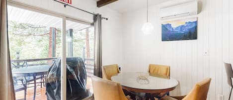 A room with a round table, four chairs, an exit sign, a painting, and a ceiling light fixture.
