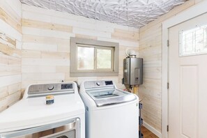 Ein Waschraum mit zwei Waschmaschinen, einem Trockner und einem Warmwasserbereiter.