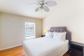 Ein Schlafzimmer mit einem Bett, einem Nachttisch, einer Lampe, einem Deckenventilator und einem Fenster mit Jalousien.