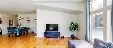 Una sala de estar amplia con piso de madera, un sofá, un televisor y un comedor con mesa y sillas.