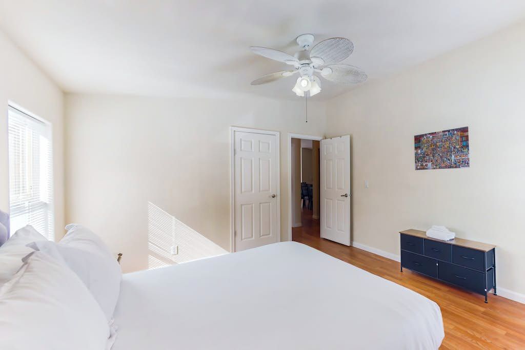 A bedroom with a bed, a ceiling fan, a dresser, and a door leading to another room.