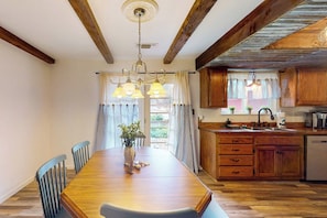 A dining area with a wooden table, chairs, and a chandelier. There is a kitchen with wooden cabinets and a sink. - The Firelight Lodge - Hot Tub & Game Room (Oakhurst)