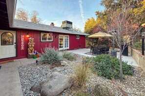 Ein rotes Gebäude mit einer Weihnachts-Bär-Dekoration, einer Terrasse mit Gartenmöbeln und einem Garten mit Steinen und Pflanzen.