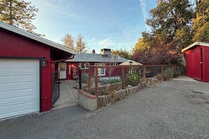 A red building with a white garage door, a fenced yard, and a small shed. - The Firelight Lodge - Hot Tub & Game Room (Oakhurst)