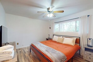 A bedroom with a bed, a ceiling fan, a window with curtains, a bedside table, and a TV. - The Firelight Lodge - Hot Tub & Game Room (Oakhurst)