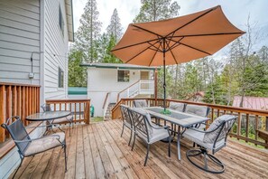 A wooden deck with outdoor furniture, including a table and chairs, and a large umbrella providing shade. - Black Bear Cabin - Boat Slip, Walk to Lake (Bass Lake)