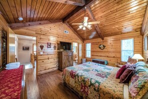 Ein Blockhausszimmer mit einem Bett, Holzwänden, einem Deckenventilator und einer kleinen Küchenzeile.